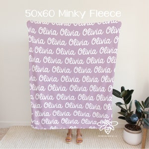 May include: A lavender minky fleece blanket with the name "Olivia" repeated in white cursive writing. The blanket is 50 inches by 60 inches.