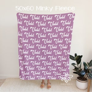 May include: A 50x60 inch minky fleece blanket with a repeating pattern of the name "Violet" in white cursive lettering on a light purple background.