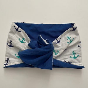 May include: A blue and white headband with a knot in the center. The headband is made of a soft, stretchy fabric and features a pattern of anchors in navy blue and teal.