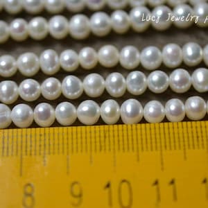 May include: Close-up of several strands of white pearls. The pearls are round and have a slight lustre. A yellow ruler with black markings is at the bottom of the image. The text "Lucy Jewelry pearls" is in the upper right corner.