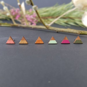 May include: Six wooden triangle earrings in various colours, including pink, green, and brown. The earrings are arranged in a row on a dark grey surface.