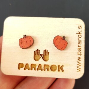 Op de afbeelding: Een paar houten pompoen oorbellen in een licht oranje kleur. De oorbellen worden getoond op een houten kaart met de tekst "PARAROK" en "www.pararok.si".