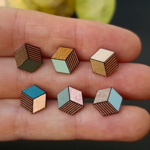 Könnte beinhalten: Sechs Holzwürfel-Ohrringe mit geometrischen Mustern. Die Würfel sind in verschiedenen Farben bemalt, darunter Türkis, Hellblau, Rosa, Gold und Braun.