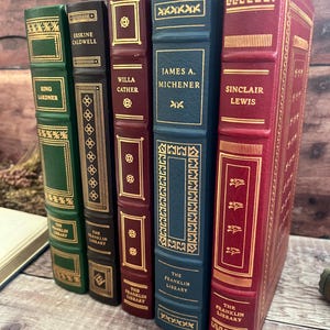 May include: Five hardcover books with gold detailing. The spines feature author names such as Ring Lardner, Willa Cather, and James A. Michener. The books are in shades of green, burgundy, and navy blue, with 'The Franklin Library' printed on the spines.