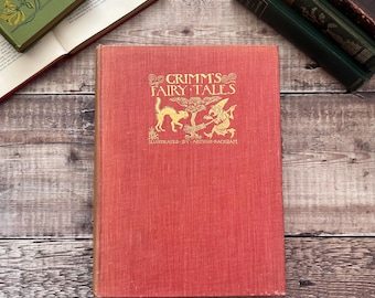 May include: A red hardcover book with the title "Grimm's Fairy Tales" in gold lettering. The book is illustrated by Arthur Rackham and features a black cat and a witch on the cover.