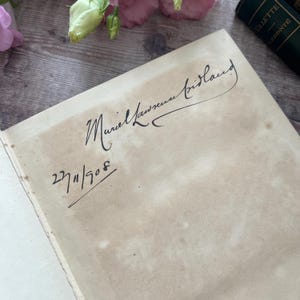 May include: A close-up of a book with a handwritten inscription that reads "Muriel Laussuer Tristany" and the date "27/1/1908".