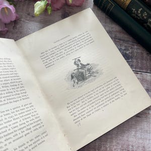 May include: A black and white illustration of a man riding a horse. The man is holding a stick in his right hand and is wearing a hat. The horse is running to the right. The illustration is from a book about the life of Oliver Goldsmith.
