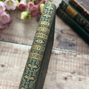 May include: The spine of a green hardback book with gold lettering that reads "The Poetical Works of Oliver Goldsmith".
