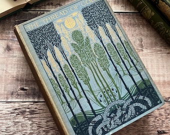 May include: Vintage book titled "The Thread of Cold" with a cover design of stylized trees in green and blue hues. The cover also features gold lettering and a design of intertwined serpents. Other books are visible in the background.