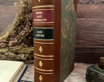 May include: A vintage edition of Jane Austen's "Sense and Sensibility". The book has a brown leather spine with gold detailing and the title in burgundy and black. The cover is decorated with a green and brown marbled pattern.