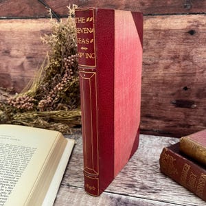 May include: A red leather-bound book with gold lettering on the spine. The title is "The Seven Seas" by Rudyard Kipling. The book was published in 1896.