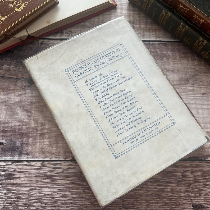 May include: A vintage book cover featuring the title "BOOKS ILLUSTRATED IN COLOUR" by Cicely M. Barker. The cover is a faded off-white with blue text and a decorative border. The book shows signs of age and wear.