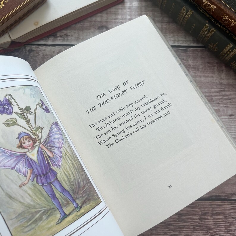 May include: An open book featuring a vintage illustration of a fairy in purple clothing holding violets. The text reads "THE SONG OF THE DOG-VIOLET FAIRY" and a poem about spring. The book is open to page 25.
