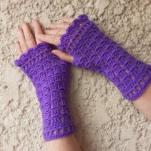 Peut inclure: Une paire de mitaines en crochet de couleur violette avec un motif ajouré. Les mitaines sont réalisées avec un point texturé et ont un bord festonné.