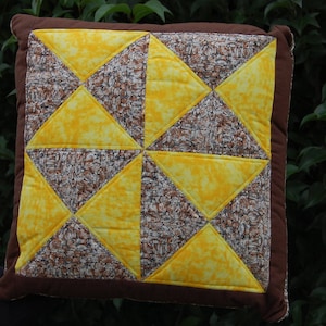 Peut inclure: Un coussin en patchwork brun et jaune avec un motif géométrique. Le coussin est composé de carrés de tissu cousus ensemble pour créer un design de type courtepointe.