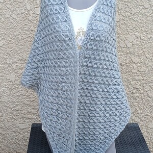 Peut inclure: Un châle en tricot bleu clair avec un motif délicat et complexe. Le châle est drapé sur un mannequin et a une forme triangulaire.