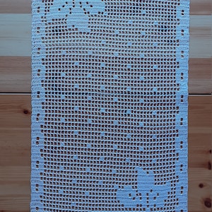 Puede incluir: Un camino de mesa de crochet blanco con un delicado patrón floral. El camino de mesa está hecho de un hilo fino y tiene un aspecto de encaje.