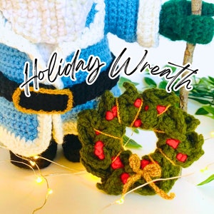 Peut inclure: Une couronne de No&euml;l en crochet de couleur verte avec des baies rouges et un n&oelig;ud dor&eacute;. La couronne est pos&eacute;e sur une surface blanche avec une figurine de P&egrave;re No&euml;l en crochet en arri&egrave;re-plan. Le texte "Holiday Wreath" est &eacute;crit en cursive noire au-dessus de la couronne.