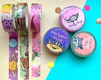 Può includere: Cinque rotoli di nastro washi colorato con diversi design. I design includono una galassia, gatti che giocano, una lucciola, un sole e un gatto con la lana. Il testo sul nastro recita "Firefly Post", "Solar System Friends" e "Cats at Play".
