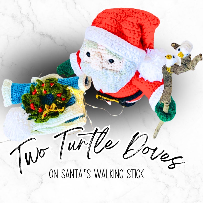 Peut inclure: Poup&eacute;e de No&euml;l en crochet repr&eacute;sentant le P&egrave;re No&euml;l tenant une canne avec deux colombes en crochet perch&eacute;es sur le dessus. Le texte "Two Turtle Doves on Santa's Walking Stick" est situ&eacute; sous la poup&eacute;e.
