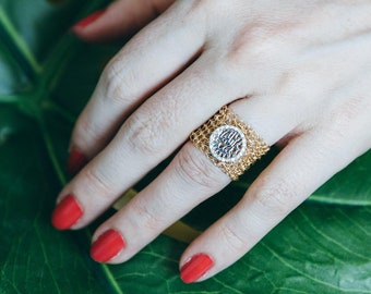 May include: A hand wearing a gold ring with a circular design and a gold bracelet with a circular design. The hand is resting on a large green leaf.