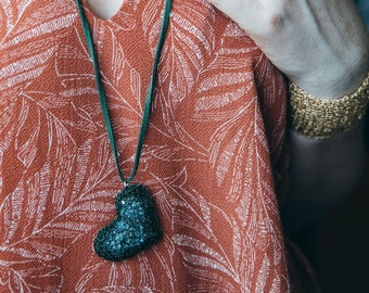 May include: A woman wearing a red and white floral dress with two necklaces. One necklace has a gold heart pendant and the other has a green heart pendant.