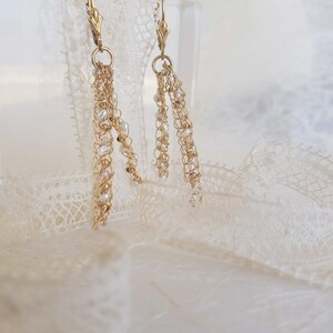 Puede incluir: Pendientes colgantes dorados con delicadas cadenas y peque&ntilde;as perlas blancas. Los pendientes presentan un cierre de palanca y un dise&ntilde;o en cascada, creando un aspecto elegante y con gracia. Los pendientes est&aacute;n sobre un fondo suave y neutro.