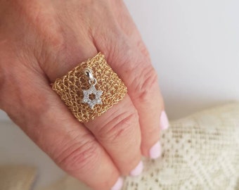 Pode incluir: Um anel de ouro com um pingente de estrela de David. O anel é feito de fio tecido e o pingente é adornado com pequenas pedras transparentes.