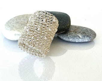 May include: A silver crocheted cuff bracelet with small beads woven into the design. The bracelet is displayed on top of three smooth stones.