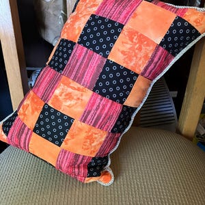 May include: A patchwork cushion with orange, black and pink fabric squares. The cushion has white piping around the edges.