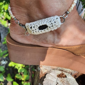 May include: White crocheted anklet with a white beaded chain and a silver clasp. The anklet is worn on a person's ankle.