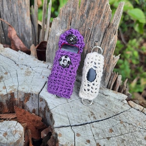 May include: Two crocheted mask extenders, one purple and one white, with a black button on the purple extender and a silver hook on the white extender.