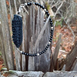 May include: A black beaded bracelet with silver accents and a black woven tassel charm.