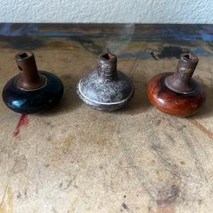 May include: Three antique cabinet knobs with metal stems and wooden or painted bases. The knobs are in shades of black, gray, and brown. The knobs are likely vintage or repurposed.