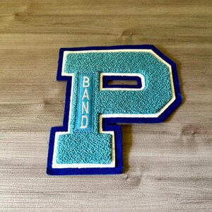 May include: A varsity-style letter P patch featuring a textured teal chenille surface with a white border and a dark blue outer edge. The vertical bar of the letter contains the word BAND embroidered in white capital letters on a teal background.