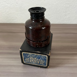 May include: A vintage brown glass viewer with a black eyepiece, resting on a black box with the text "ULTRAVUE" in a blue and white label. The viewer has the word "KODAK" embossed on it.