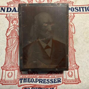 May include: A vintage portrait of a man in a dark suit and bow tie, set within a dark rectangular frame. The frame is secured with small metal rivets. The background features the words "STANDARD POSITIONS" and "THEO. PRESSER".