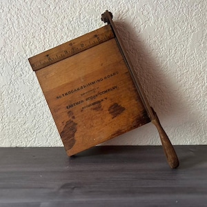 May include: Vintage wooden Kodak trimming board with a ruler along the top edge. The board has a blade and a wooden handle. The text "No 1 Kodak Trimming Board" and "Eastman Kodak Company" are visible on the board.
