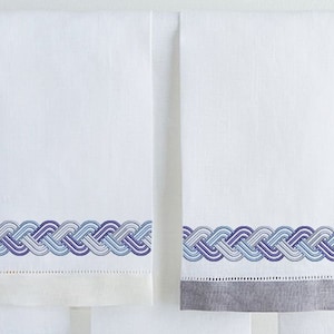 May include: Two white hand towels with a blue and gray woven border design. The towel on the right has a gray hem.