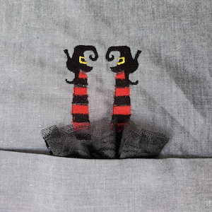 May include: Two black and red striped witch figures with yellow eyes and black hats, standing on a black tulle skirt.