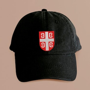 May include: Black baseball cap with a curved brim. The cap features a red and white emblem on the front. The emblem is a shield with a cross and four stylized 'C's.