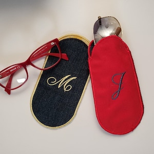May include: Two personalized eyeglass cases, one red with the letter "J" embroidered in navy blue and one navy blue with the letter "M" embroidered in gold.