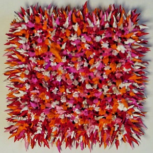 May include: A square-shaped wall art piece made of small, pointy, colourful shapes. The shapes are in shades of red, orange, pink, and white.