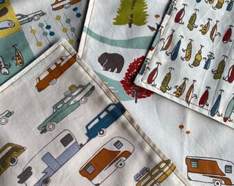 May include: A collection of square fabric coasters with various retro-style travel and nature-themed patterns. Designs include cars, campers, trees, and abstract shapes in shades of blue, brown, green, and red. Each coaster has a stitched border.