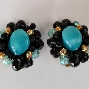 May include: A pair of turquoise and black clip-on earrings with a cluster of beads. The earrings feature a large turquoise cabochon surrounded by black beads and smaller turquoise beads.