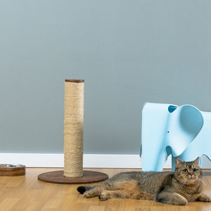 May include: A brown cat scratching post with a sisal rope covering, a blue elephant-shaped stool, and a brown tabby cat lying on the floor.