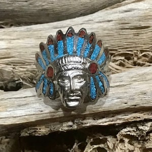 May include: A silver ring featuring a turquoise and red stone inlay depicting a Native American chief wearing a headdress.