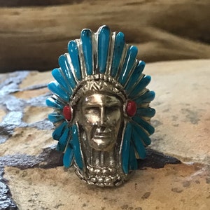 May include: A silver ring with a turquoise and red stone design depicting a Native American chief wearing a headdress.