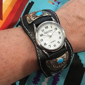 May include: A black leather cuff watch with silver accents and turquoise stones. The watch face is white with black numbers and the words "SelecTime" and "Quartz".