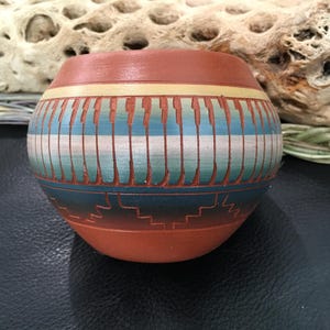 Könnte beinhalten: Eine kleine, handbemalte Töpferschale mit einem geometrischen Muster in Blautönen, Grün und Weiß auf einem roten Tonuntergrund.
